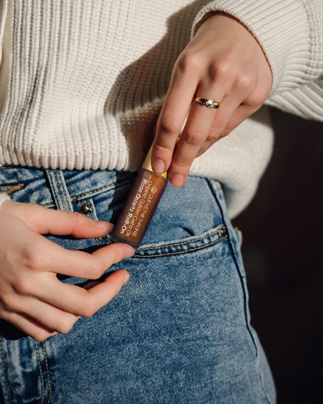 A woman slipping a Queen of the Thrones castor oil rose quartz roll-on into her jeans pocket